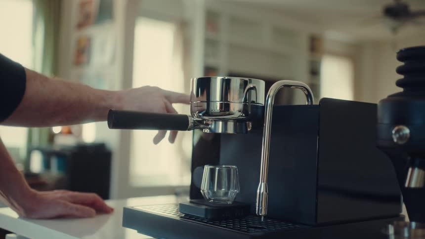A person locks a portafilter into a modern espresso machine and presses a button to begin brewing a shot