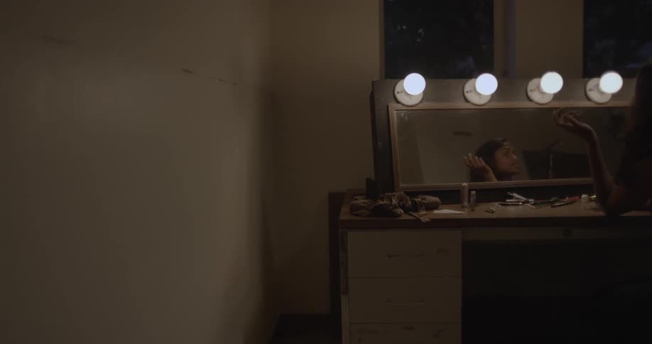 Woman sits at vanity and plays with her hair