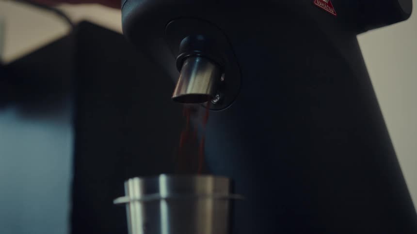 Slow motion close up of a coffee grinder dispensing fresh coffee grounds into a metal cup
