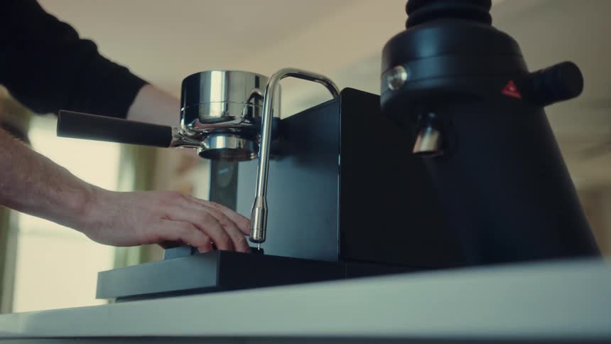 A man prepares to brew an espresso shot in slow motion, locking the portafilter into the sleek machine on a modern kitchen counter