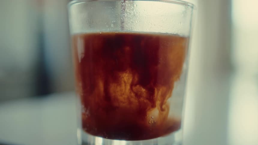 Mesmerizing slow-motion close-up of espresso being poured into a glass of sparkling water with ice