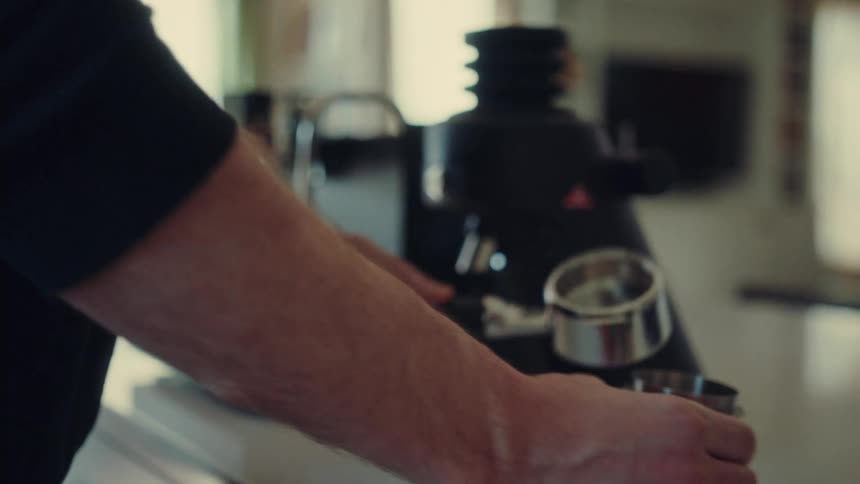 A barista meticulously cleans a portafilter and prepares freshly ground coffee for an espresso in slow motion