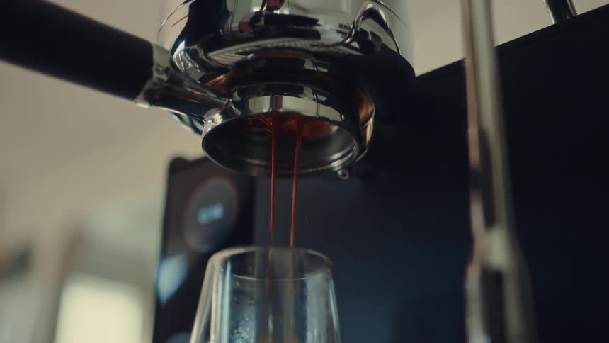 A close-up slow-motion shot of rich espresso dripping from a portafilter into a glass cup