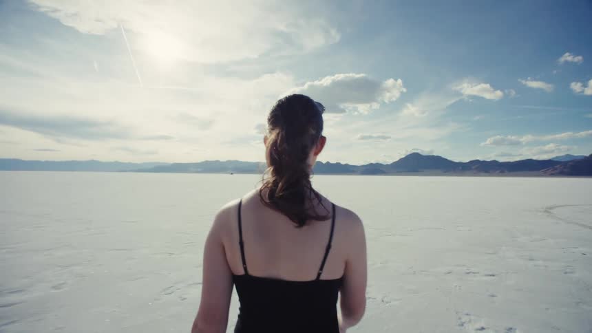 A young woman walks in slow motion across the vast expanse of the Bonneville Salt Flats
