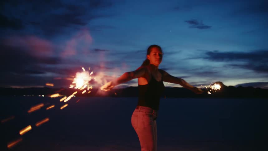 A free-spirited woman creates mesmerizing light trails as she dances with sparklers in the vast desert at twilight