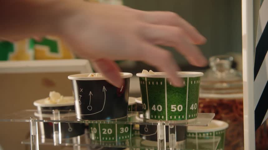 A hand grabs a football-themed cup of popcorn from a snack stand during a game day party