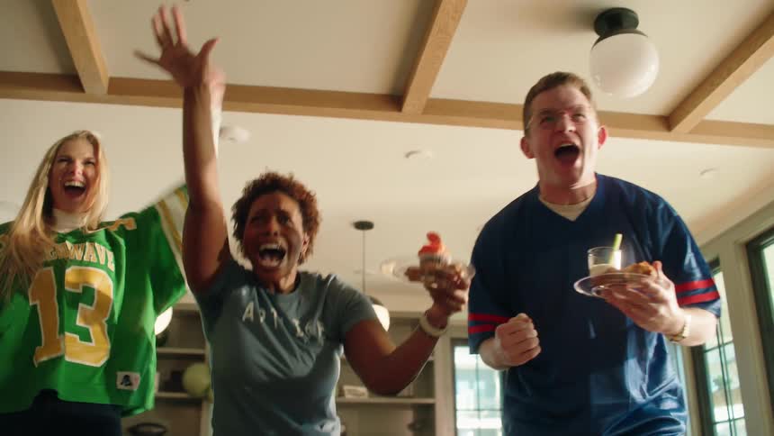 Excited football fans jump up from the couch and cheer wildly while watching the big game at a party