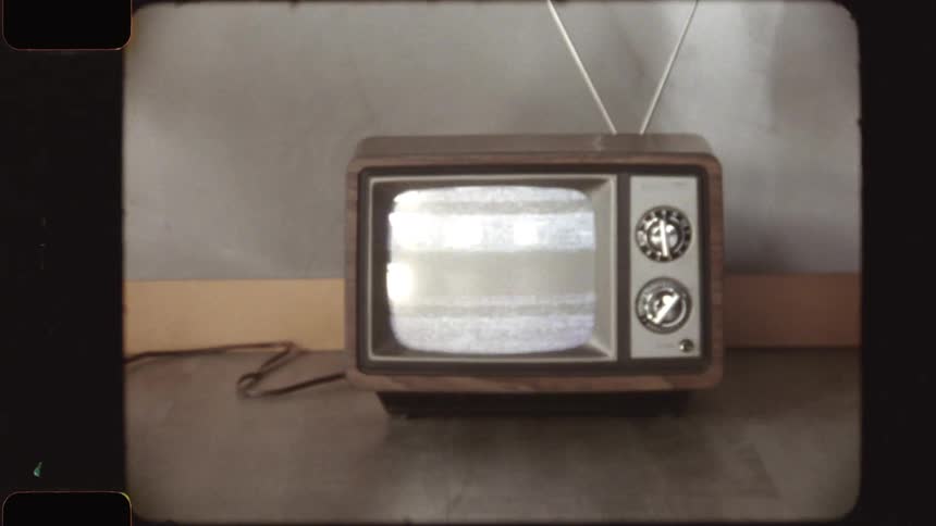 Vintage 8mm footage of a retro television displaying static, zooming out to show the set on the floor before zooming back in