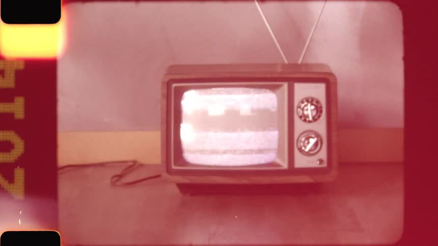 Slow zoom out from a vintage wood grain television showing static, with an authentic old film look including sprocket holes, light leaks, and a film burn out
