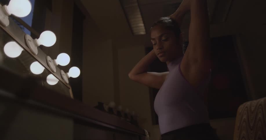 A female dancer is doing her hair in a dressing room