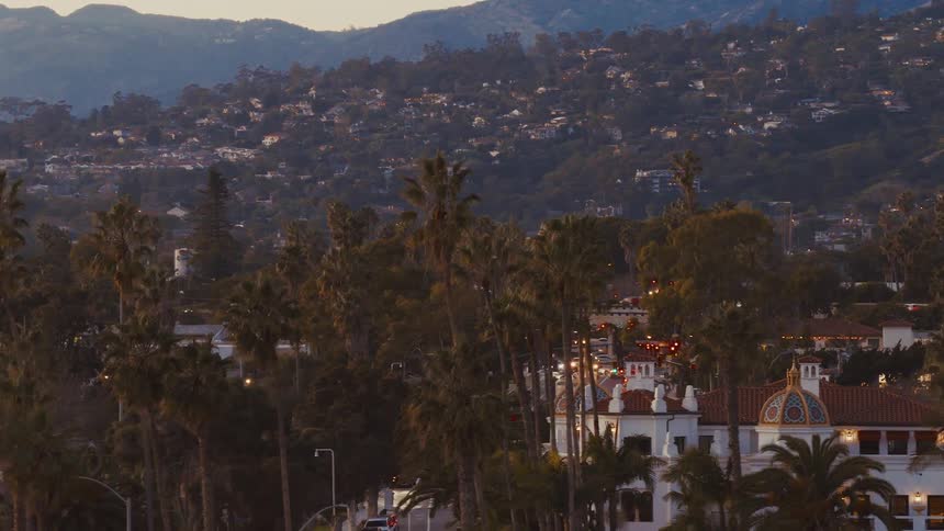 An idyllic view of a coastal California city with Spanish architecture and palm-lined streets at twilight as the foothills glow