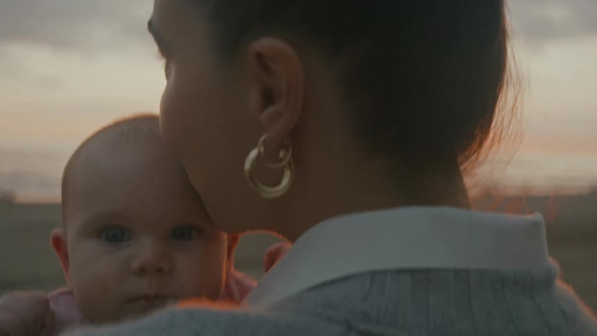 A mother tenderly holds and kisses her baby on the beach during a beautiful golden sunset