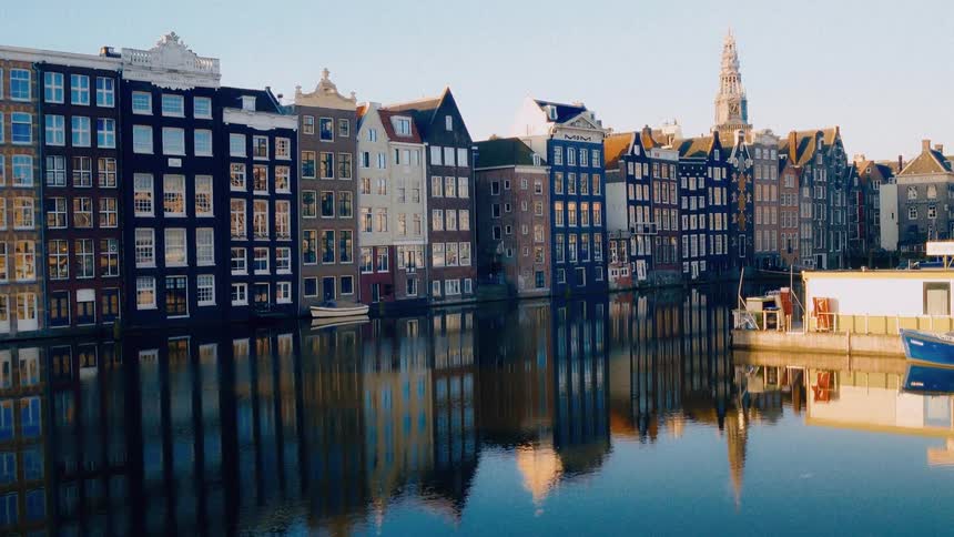A scenic, static shot of colorful traditional canal houses perfectly reflected in the calm waters of an Amsterdam canal
