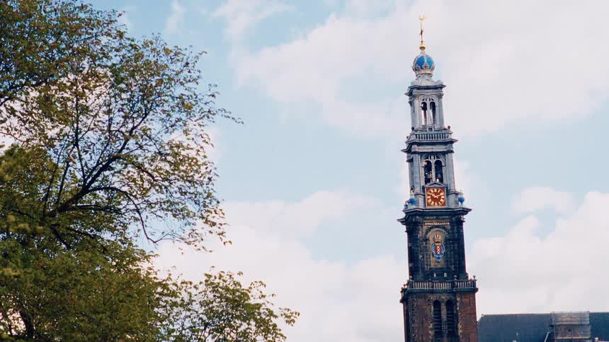A low angle shot of the historic Westerkerk church tower in Amsterdam, Netherlands, with a tree in the foreground