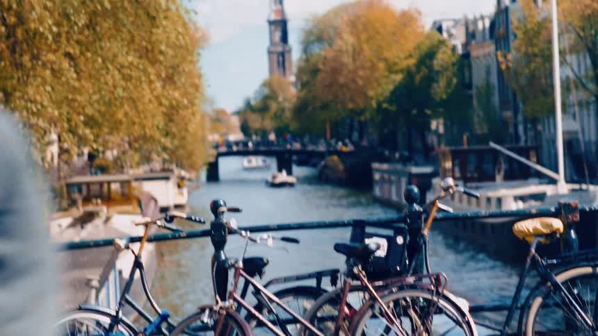 Bicycles line a bridge railing overlooking a picturesque Amsterdam canal with boats and historic architecture on a beautiful autumn day