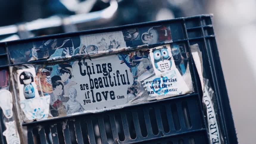 A slow rack focus reveals a thoughtful quote, 'Things are beautiful if you love them,' on a sticker-covered crate on a bicycle