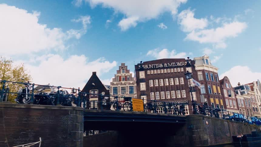 A picturesque view from a boat on an Amsterdam canal reveals a classic bridge lined with bicycles and historic Dutch buildings