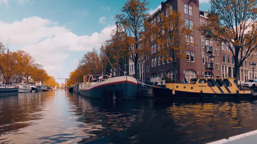 A slow cinematic journey backwards along a picturesque Amsterdam canal reveals classic Dutch architecture and moored houseboats on an autumn day