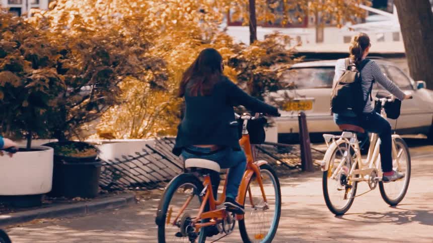 A group of friends enjoy a scenic bike ride down a city street lined with golden autumn trees in slow motion