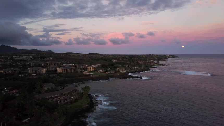 Sun setting in the distance of ocean side town on cloudy evening