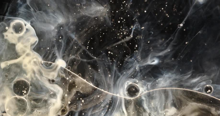 A mesmerizing macro shot of milky white liquid and shimmering particles swirling in a dark fluid, creating an abstract cosmic scene