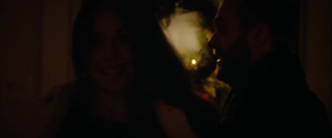 A romantic couple shares an intimate kiss and a warm embrace in a dimly lit room decorated for the holidays