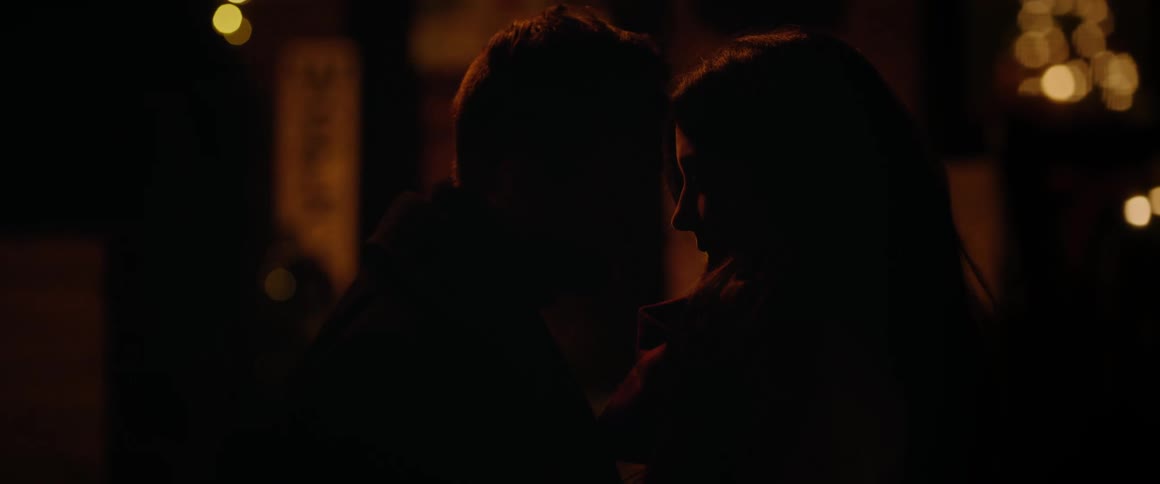 A silhouetted couple shares an intimate and tender embrace on a warmly lit porch decorated for the Christmas holidays