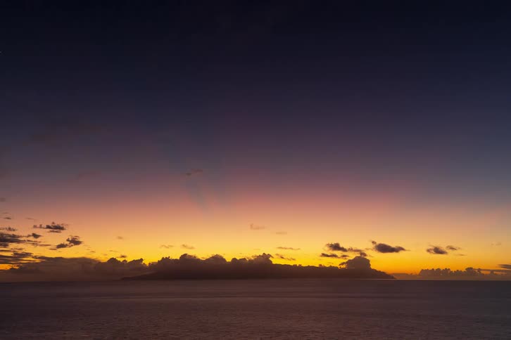 A beautiful time-lapse of a colorful sunset over a tranquil ocean with a distant island silhouetted against the horizon