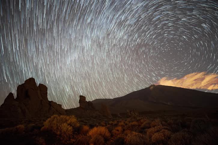 A mesmerizing timelapse captures star trails forming a celestial vortex over a volcanic desert landscape