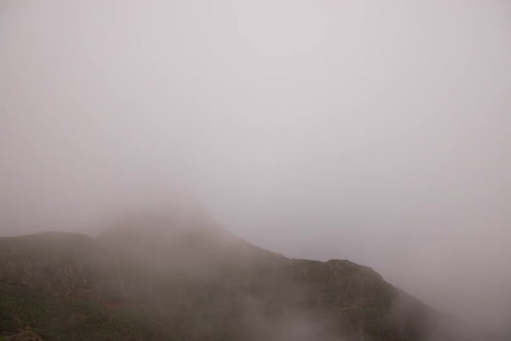 Dense white fog completely engulfs a lush green mountain until nothing is visible