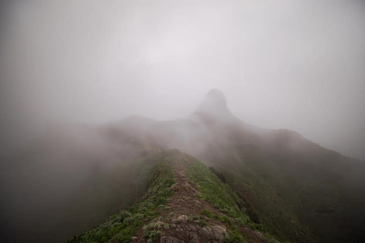 A dramatic time-lapse of a lone hiker walking along a foggy green mountain ridge as clouds roll over the peaks