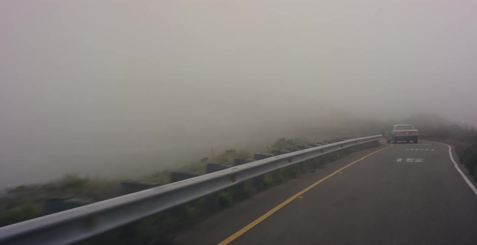 A point-of-view drive along a steep and winding coastal highway enveloped in thick, mysterious fog