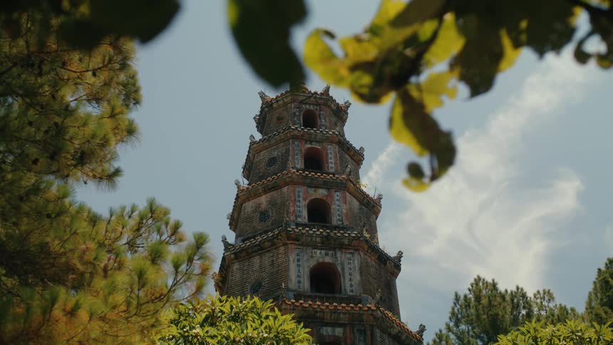 A low-angle view of the historic Thien Mu Pagoda in Vietnam, framed by lush green trees against a bright sky