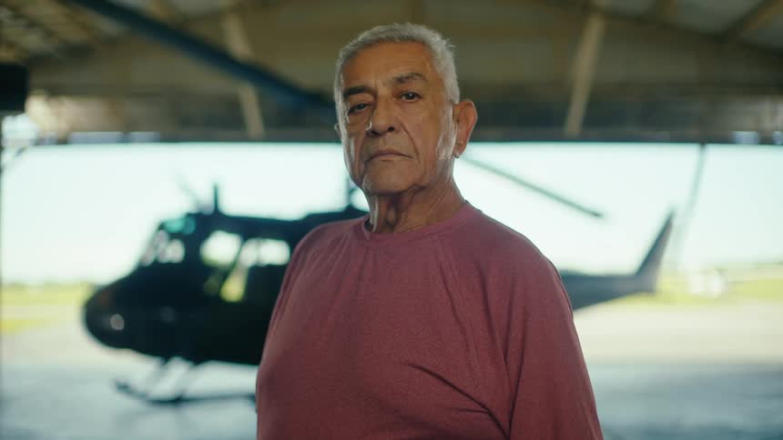 Portrait of a serious elderly man standing in an aircraft hangar with a helicopter in the background