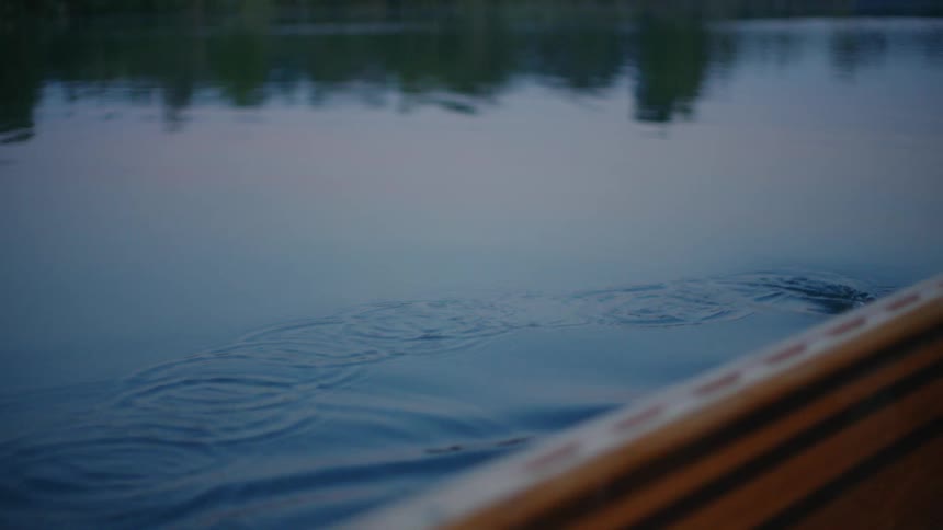 Close up in slow motion of a wooden canoe paddle dripping water and creating ripples on a serene lake at dusk