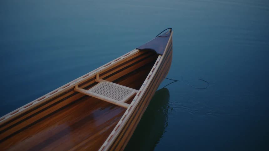 A beautifully crafted wooden canoe sits peacefully on calm blue water at dusk