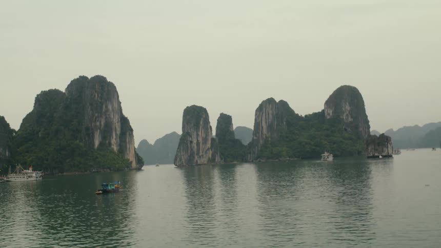 A serene, wide view of the iconic limestone karsts and jungle-covered islands of Ha Long Bay, Vietnam, with boats on the calm water