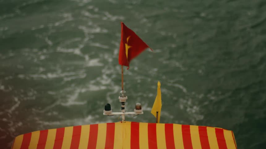 A Vietnamese flag waves in the wind on the top of a boat as it sails through the water