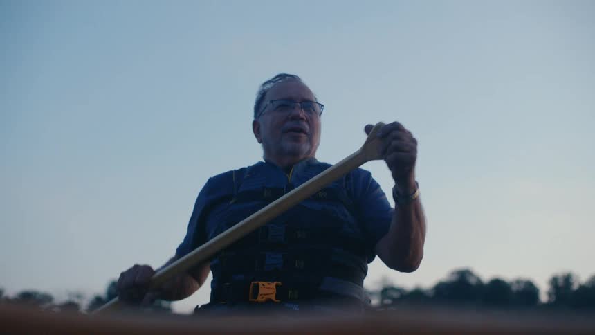 A serene slow-motion low angle shot of an older man paddling his canoe at twilight