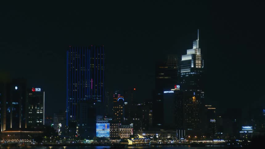 A slow zoom into the glowing Ho Chi Minh City skyline at night with boats passing on the Saigon River