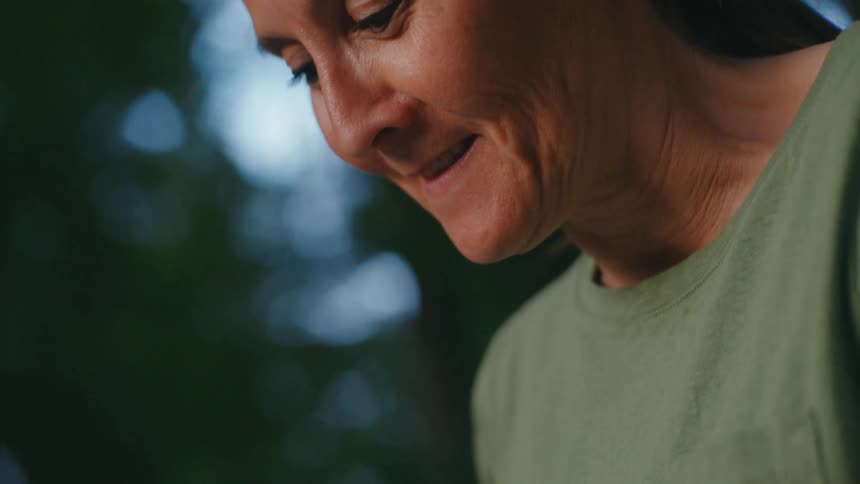 A slow-motion close-up reveals a smiling middle-aged woman reading a sentimental, handwritten letter outdoors