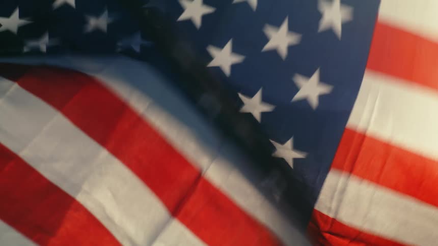 A dynamic close-up shot of the American flag waving proudly in the wind against a sunlit sky
