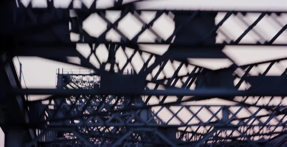 A disorienting abstract shot of a steel bridge's intricate latticework moving past at high speed