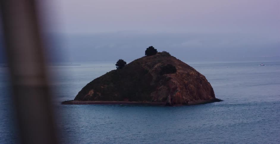 A contemplative view of a small, solitary island from a moving vehicle on a gray, overcast day