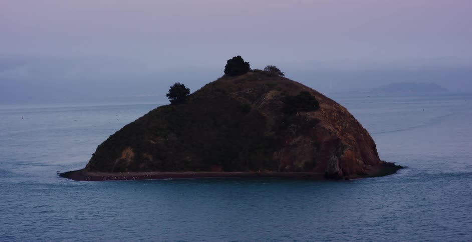 A serene view of a small, isolated island sitting in the bay during a moody, overcast twilight