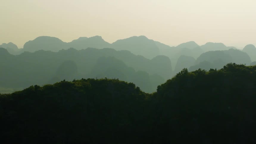 Lush, layered mountain silhouettes fade into the distance under a soft, hazy sky