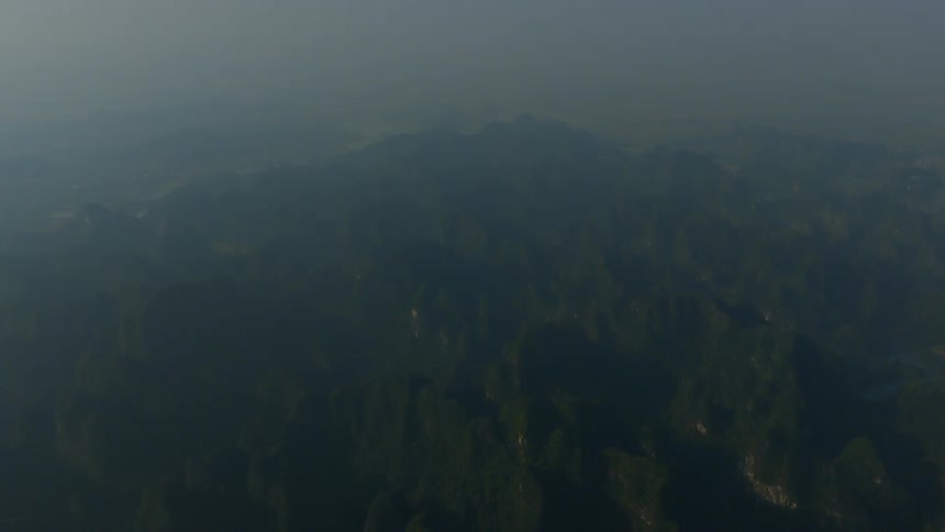 A static aerial shot of a vast, hazy mountain range covered in green forests