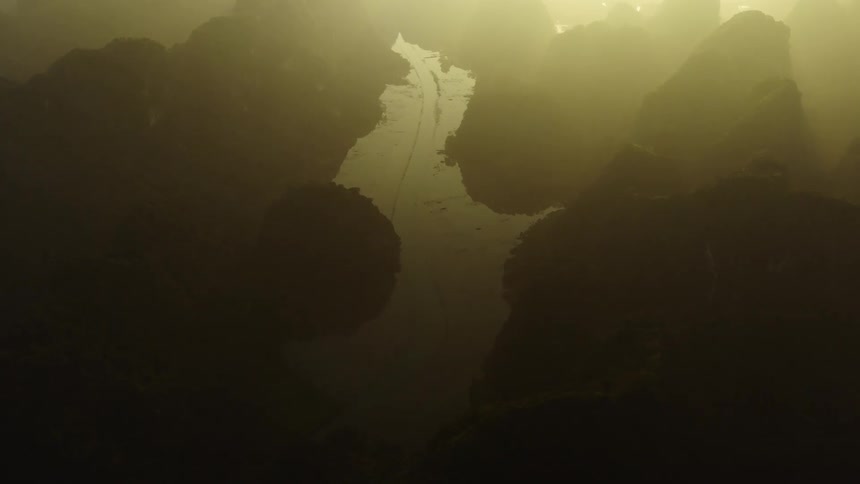 An ethereal aerial shot pulls back through a golden misty river valley surrounded by majestic karst mountains