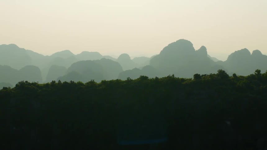 A serene view of layered mountain silhouettes fading into the hazy horizon above a dark, forested landscape