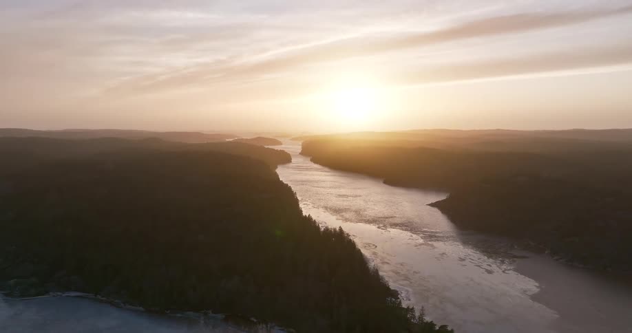 An expansive aerial view captures the sun rising over a frozen river winding through a vast, tree-covered wilderness